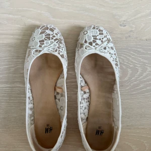 Vita spetsballerinor från H&M - Söta vita ballerinaskor från H&M i spets med blommigt mönster och liten rosett framtill. Skorna har rund tå och platt sula. Lätta och luftiga, passar till både jeans och klänning.