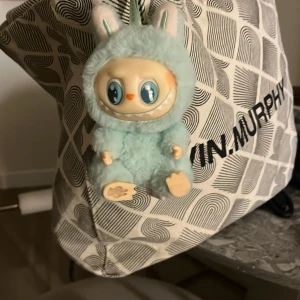 En Labubu - En söt ljusgrön labubu. Han hänga den på en väska, rummet eller ha den som gosedjur 🧸. Är från POP MART. Den är ganska liten och den är et monster men en gulligt monter😊