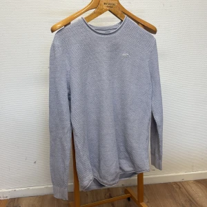 Ljusgrå stickad tröja från Hollister - Säljer en ljusgrå stickad tröja från Hollister med diskret logga på bröstet. Tröjan har rund halsringning och lång ärm, perfekt för lager-på-lager. Mjuk och skön struktur som ger en avslappnad vibe.