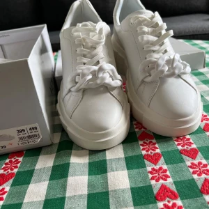 Vita chunky sneakers från Venice - Säljer ett par vita chunky sneakers från Venice med cool kedjedetalj framtill. Skorna har snörning, plattformsula och är tillverkade i syntetmaterial. Perfekta för dig som vill sticka ut med en trendig och fräsch look.