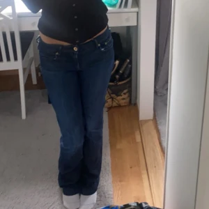 Mörkblå bootcut jeans låg midja - Säljer ett par mörkblå jeans med låg midja och bootcut-modell. Jeansen har klassisk femficksdesign och stängs med knapp och dragkedja. Perfekta för dig som gillar en tidlös och avslappnad look. De är slitna längs ner, skriv för bild 💕