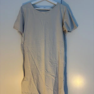 Beige t-shirtklänning från Lager 157 - Enkel och stilren beige t-shirtklänning från Lager 157 i 100% bomull. Modellen är rak med korta ärmar och rund halsringning, perfekt för en chill och avslappnad look. Passar dig som gillar basic och comfy vibes.