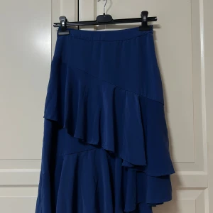 Blå volangkjol  - Supersnygg blå långkjol  volangdetaljer i flera lager. Kjolen har en asymmetrisk design som ger en cool och flowy look.  Som ny