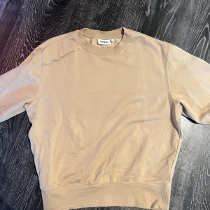 Beige sweatshirt från Weekday - En stilren beige sweatshirt från Weekday med rund halsringning och långa ärmar. Tröjan har en relaxed passform och är gjord i mjuk bomull, perfekt för en chill och enkel look. Passar till allt och är superenkel att matcha med jeans eller kjol.