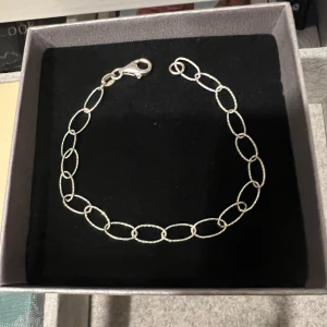 Silver kedjearmband med ovala länkar - Stilrent armband i silver med stora ovala länkar och karbinlås. Kedjan har en lätt texturerad yta som ger extra glans och en modern känsla. Perfekt för att ge din outfit en cool touch.