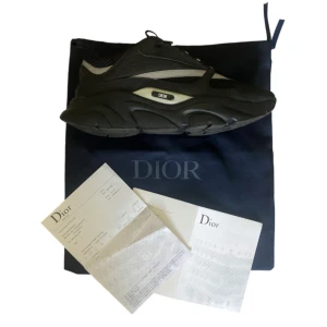 Svarta Dior B22 - Chunky svarta sneakers från Dior med cool design och tydlig Dior-logga på sidan. Skorna har en kraftig sula, meshdetaljer och inslag av syntetmaterial. Perfekta för dig som gillar statement-sneakers med exklusiv känsla.