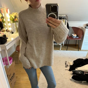 Beige stickad polotröja i loose fit - Supermysig beige stickad polotröja med ribbade muddar och hög hals. Tröjan har en loose passform och långa ärmar, perfekt för lager på lager under kyliga dagar. Enkel och stilren design som funkar till jeans eller kjol. Har aldrig använt tröjan💕