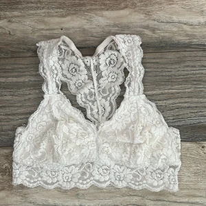 Vit spets bralette med blommönster - Superfin vit bralette i spets med blommigt mönster och bred spetskant. Modellen är ärmlös och har racerback i spets, vilket ger en snygg och feminin look. 