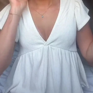 Vit omlottopp från Gina Tricot - Supersöt vit topp från Gina Tricot med v-ringning och omlottdetalj. Toppen har korta puffärmar och är tillverkad i ett ribbat bomullstyg. Den har en flowy, luftig passform och är perfekt för varmare dagar.