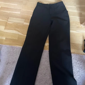 Svarta kostymbyxor med raka ben - Snygga svarta kostymbyxor med raka ben och klassisk passform. Byxorna har diskreta fickor i sidorna och stängs med knapp och dragkedja. Perfekta för en clean och stilren look.