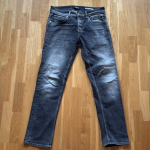 Replay Grover straight fit jeans - Säljer ett par Replay Grover jeans i straight fit. De är mörkgrå med snyggt slitna detaljer och klassisk femficksdesign. Jeansen har normal passform och är tillverkade i mjukt denimtyg med Replay-logga på fickan och läderpatch bak.