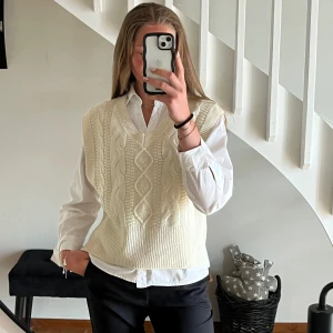 Vit  kabelstickad väst - Snygg vit stickad väst med klassiskt kabelstickat mönster och v-ringning. Perfekt att bära över en skjorta för en stilren outfit.🥰