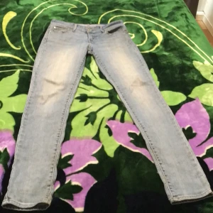 Levi's Demi Curve Skinny ljusblå jeans - Ljusblå Levi's Demi Curve Skinny jeans med klassisk femficksdesign och dragkedjegylf. Snyggt slitna detaljer och smal passform som sitter tajt hela vägen ner. Perfekta för dig som gillar en modern och clean look.