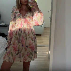 Blommig kortklänning med volang - Superfin kortklänning med blommigt mönster. Klänningen har v-ringning och volangdetalj vid halsen💞använt en gång