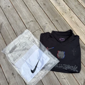FC Barcelona x Nike svart fotbollströja - Säljer en svart FC Barcelona x Nike fotbollströja med coola Travis Scott Cactus Jack-detaljer. Tröjan har korta ärmar, röd och blå sidopanel, klubbmärke på bröstet och tryck på ryggen. Materialet är lätt och andas, perfekt för match eller träning. Pris kan diskuteras vid snabb affär 