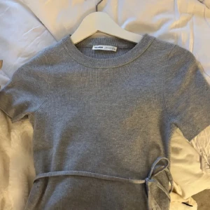 Grå ribbad topp med knyt från Pull&Bear - Säljer en ljusgrå ribbad topp från Pull&Bear med korta ärmar och croppad passform. Toppen har ett snyggt knytband i midjan som ger en extra detalj. Perfekt till jeans eller kjol för en chill och trendig look. skickar bara om du följer mig💞
