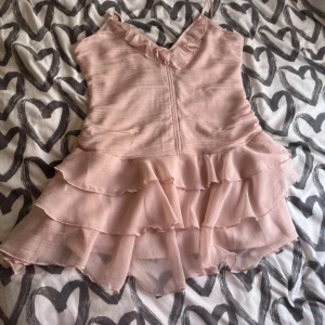 Ljusrosa volangklänning från hm - Rosa klänning från hm. Storlek M, inte stretchig, använd 1 gång. Det finns en dragkedja på ryggen och man kan inte göra banden kortare.