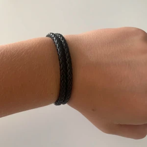 Svart flätat armband Fritz Olsson - Stilrent svart armband från Fritz Olsson i flätat material med silvriga metalldetaljer. Snyggt och enkelt att matcha med andra accessoarer. Kommer i original ask.