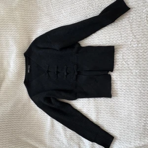 Stickad kofta med knappar från H&M - Två stickade koftor från SHEIN  i svart och vitt. Båda har lång ärm, ribbad struktur och unika dekorativa knappar framtill. Snygg v-ringning och croppad passform som ger en trendig look. Perfekt att styla med jeans eller kjol för en cool vardagsoutfit jag säljer båda dom två för 100kr eller 1 för 50kr styck.