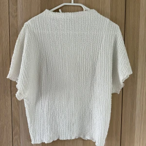 Vit strukturerad topp från Zara - Säljer en vit topp från Zara i storlek S. Toppen har en cool strukturerad yta med korta ärmar och avslappnad passform. Perfekt för dig som gillar en enkel men ändå unik look. Superlätt att matcha med både jeans och kjol.