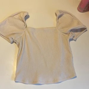 Beige topp från H&M - Superfin beige ribbad topp från H&M med puffiga korta ärmar och fyrkantig halsringning. 