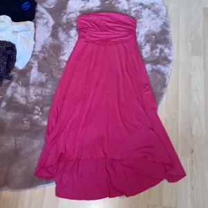Rosa långklänning - Säljer en axelbandslös rosa klänning från Bodyflirt i storlek 38. Klänningen har en snygg omlott-effekt upptill och är längre bak än fram för en cool look. Perfekt för dig som vill sticka ut med en färgstark och feminin stil.