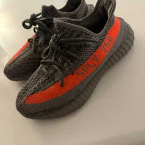 Adidas Yeezy Boost 350 V2 Beluga - Säljer ett par Adidas Yeezy Boost 350 V2 Beluga med grå och orange Primeknit-överdel, ikonisk SPLY-350 text på sidan och ribbad sula. Skorna har snörning och en riktigt skön, chunky vibe. Perfekta för dig som vill sticka ut med streetstyle.