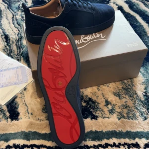 Mörkblå  Christian Louboutin - Snygga mörkblå sneakers från Christian Louboutin med ikonisk röd sula och diskret logga på hälen. Skorna har rund tå, snörning och är tillverkade i mocka med läderdetaljer. Perfekta för dig som vill sticka ut med exklusiv stil.