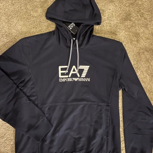 Mörkblå hoodie Emporio Armani - Mörk blå hoodie från Emporio Armani EA7. Oanvänd med tags i storlek M. Säljer då den inte passar mig 