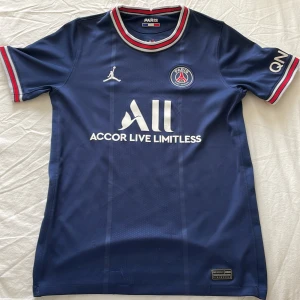 Messi Tröja 2022 - Paris Saint-Germain fotbollströja med Messi 30-tryck på ryggen. Mörkblå med vita detaljer, röda och vita ränder på krage och ärmslut. PSG-emblem och Jordan-logga på bröstet. Tillverkad i lätt och ventilerande polyester, perfekt för fotbollsplanen. Köpt från unisport säsongen 2022 Tröjan säljs inte mer Pris kan diskuteras!