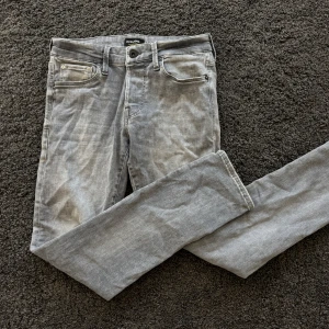 Grå jeansbyxor från Jack & Jones - Säljer ett par grå jeansbyxor från Jack & Jones med klassisk femficksdesign och raka ben. Byxorna har slim/glenn passform och är tillverkade i ett mjukt jeanstyg. Perfekta för en avslappnad stil.w29,30