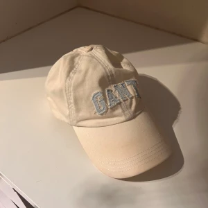 Keps från GANT - Snygg vit keps från GANT med broderad logga framtill i ljusblått. Klassisk böjd skärm och justerbar passform bak. Perfekt accessoar för en avslappnad och stilren look. Kepsen är ren och fräsch då den blivit tvättad innan försäljning 🫧🧼✨