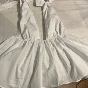 Vit kort omlottklänning med knyt - Supersöt vit festtop med djup v-ringning och breda axelband som knyts i nacken. Perfekt för sommaren. Den är aldrig använd men den är testad engång.