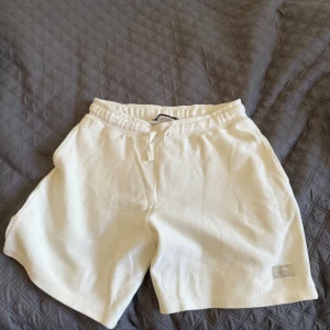 Vita shorts från Zara med snörning - Pris kan diskuteras! Snygga vita shorts från Zara i medium med skön, lite grovstickad struktur. De har elastisk midja med snörning och en liten patch med text på benet. Perfekta för chill dagar eller när du vill ha en clean look. Den har använt många gånger under sommaren men den ser som ny ut!