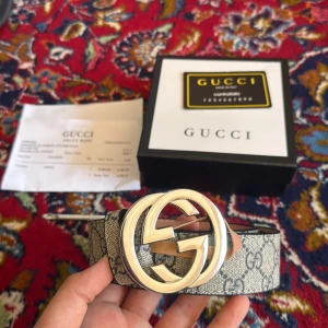 Bälte - Säljer ett snyggt bälte i beige med en silver-logga. Bältet är gjort i skinn och har exklusiv känsla. Perfekt för dig som vill sticka ut med en ikonisk accessoar.