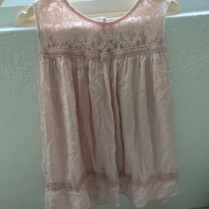 Ljusrosa spetsblus Made in Italy - Supersöt ljusrosa blus med spets upptill och fina virkade detaljer. Ärmlös modell med knäppning bak och lätt, flowy passform. Perfekt för dig som gillar romantisk och feminin stil. Blusen har rund halsringning och vackra spetsmönster.