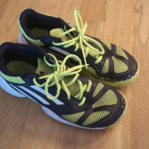 Adidas inomhus sneakers gul och svart strl 39⅓ - Snygga Adidas sneakers i svart och neongult med vita detaljer och märkning 'ADITUFF' på sidan. Ovandelen är i mesh och syntet för bra ventilation. Skorna har snörning och en slitstark sula. Perfekta för dig som gillar sportig stil.
