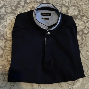 Mörkblå pikétröja från Massimo Dutti - Snygg mörkblå pikétröja från Massimo Dutti med korta ärmar och stilren krage i ljusblått. Tröjan har  en klassisk passform som funkar till många looks. Perfekt för dig som gillar en clean och modern stil. Storlek L men passar även M