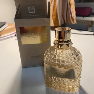 Valentino Uomo Born In Roma The Gold 60ml kvar - Lyxig parfym från Valentino, Uomo Born In Roma The Gold. Flaskan är i transparent glas med nitar och guldiga detaljer, samt en guldig etikett framtill. Designen är exklusiv och flaskan har en cool, kantig form som sticker ut i badrumshyllan.