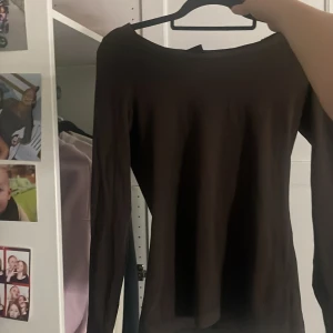 Mörkbrun långärmad topp - En stilren mörkbrun långärmad topp med rund halsringning. Enkel och clean design utan synliga detaljer eller mönster, perfekt att matcha med olika outfits. Materialet känns mjukt och följsamt mot kroppen.
