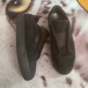 Axel Arigato skor - Stilrena svarta sneakers från Axel Arigato i mocka med diskret guldtext på sidan. Skorna har platt sula och rund tå, perfekt för en clean och modern look. Passar till det mesta och är lätta att matcha. Ny skick, skriv för mer bilder o info ℹ️ 