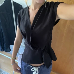 Svart omlottopp med knyt - Säljer en svart omlottopp med knyt i sidan och v-ringad hals. 