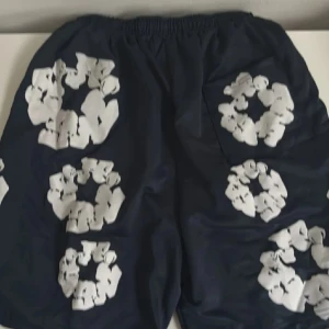 denim tears shorts - Snygga mörkblå denim tears shorts med vita blommiga tryck över hela tyget. De har elastisk midja med snörning för skön passform. Perfekta för sommardagar och chill häng. Materialet känns lätt och luftigt. Säljer endast för 429 men kom gärna med förslag tack!