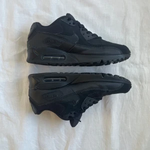 Nike Air Max 90 Triple Black sneakers - Snygga Nike Air Max 90 i helsvart färg. Skorna har en chunky sula med synlig Air Max-dämpning, mesh och skinnpaneler samt klassisk snörning. Perfekta för dig som gillar en clean och sportig look med streetkänsla.