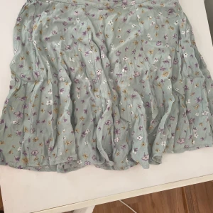 Blommig mintgrön kortkjol - Supersöt kortkjol från New Look i mintgrönt tyg med små blommor i lila, vitt och gult. Kjolen har en lätt volangig form och är perfekt för varma dagar. Tunn och luftig, passar dig som gillar en romantisk och chill stil.