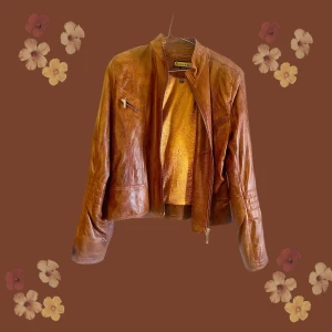 Brun skinnjacka från D'ecelli, stl 40 - Snygg brun skinnjacka från D'ecelli med guldfärgat innerfoder. Jackan har en klassisk rak passform, ståkrage och dragkedja framtill samt en bröstficka med dragkedja. Perfekt för dig som vill ha en tidlös och cool look.