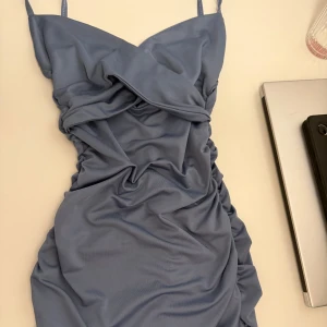 Ljusblå kort klänning med rynk - Supersnygg ljusblå kort klänning med smala axelband och rynkade detaljer framtill och baktill. Klänningen har en figurnära passform och är tillverkad i ett mjukt, stretchigt material som känns bekvämt mot huden. Perfekt för dig som vill sticka ut med en cool och trendig look. Har aldrig haft på mig den. Ord pris 219kr.