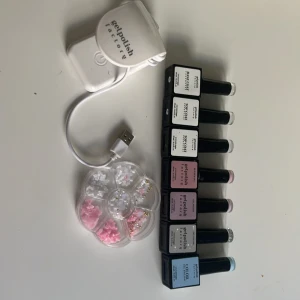 Gelpolish nagelkit med dekorationer - Komplett gelpolish nagelkit från Gelpolish Factory med sex flaskor i olika färger: ljusblå, grå, rosa och glitter. Inkluderar base coat, top coat och builder gel. Medföljer UV-lampa och ett hjul med söta nageldekorationer i vitt, rosa och guld.
