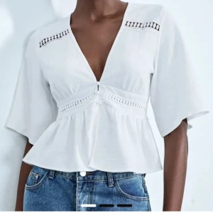 Vit blus med v-ringning  - Superfin vit blus med djup v-ringning och korta ärmar. Blusen har spetsdetaljer vid axlar och en volang nertill. 