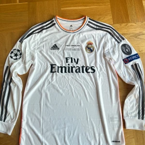 Real Madrid långärmad Ronaldo-tröja - Säljer en vit långärmad Real Madrid-tröja från Champions League-finalen 2014 med Ronaldo 7 på ryggen. Adidas, med Fly Emirates-tryck, klubbmärke och CL-patchar på ärmarna. Tunn och sportig climacool-material, svarta detaljer och orange kant vid kragen.